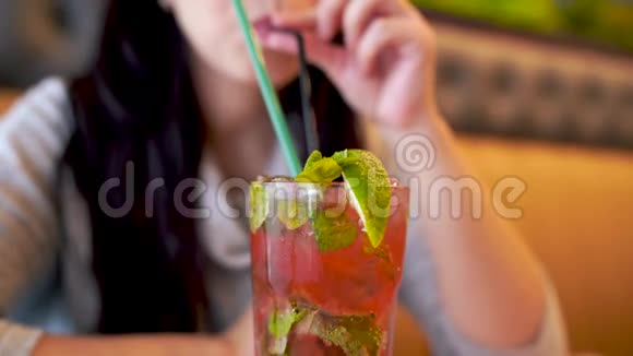 女人在咖啡馆喝鸡尾酒成年女士坐在餐桌上一边用吸管啜饮新鲜水果饮料视频的预览图