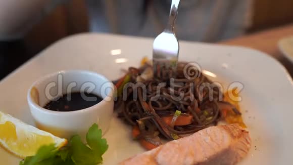 在白色盘子上用鲑鱼和酱油特写荞麦面的美味菜肴女人手捻面条视频的预览图