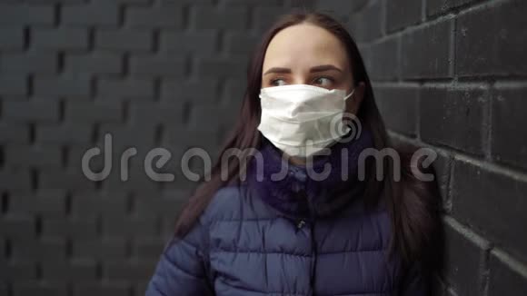 戴着医疗面具的年轻女子脸上贴着黑色砖墙的肖像成年女性用面具遮住她的脸视频的预览图