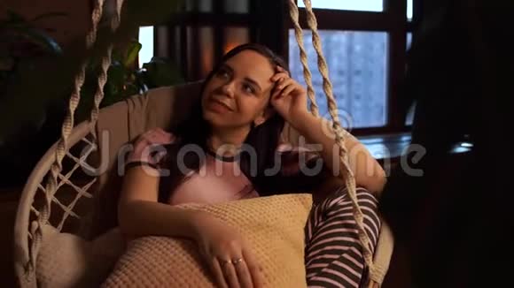 快乐的年轻女人在家里躺在吊床上年轻迷人的年轻女性坐在一起看相机视频的预览图