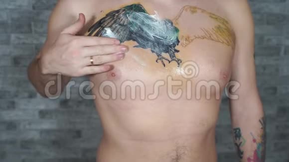 男人在胸前不完整的纹身上涂抹奶油男人的特写用手把药膏涂抹在身体的一部分视频的预览图