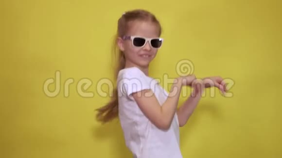 滑稽的小女孩戴着时髦的太阳镜一边跳着摆手一边在黄色背景下像兔子一样跳舞视频的预览图