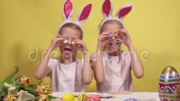 可爱的姐妹有兔子的耳朵在复活节准备的时候眼睛旁边放着五颜六色的鹌鹑蛋视频的预览图