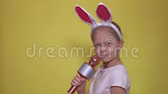 可爱的小女孩带着兔子耳朵和麦克风在复活节唱歌时微笑着看着相机视频的预览图