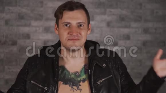 一个震惊的男人穿着一件时髦的夹克胸前有纹身背景灰色一个绝望的男人的画像视频的预览图