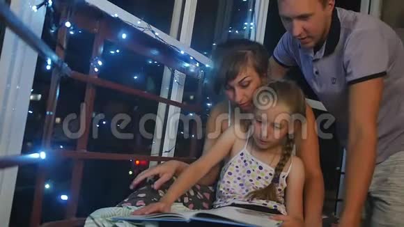 妈妈爸爸和女儿在睡觉前坐在夜窗附近女儿读了一本大童话书视频的预览图