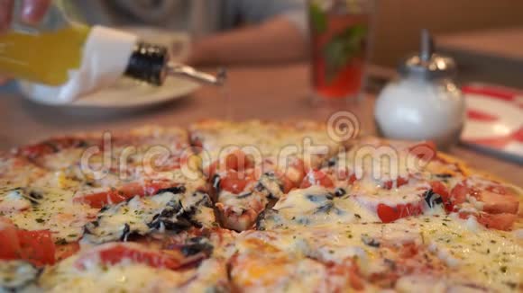 桌上摆着大披萨女人手在披萨片上撒辣橄榄油视频的预览图