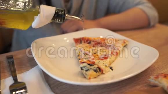 年轻女子坐在咖啡馆的桌子旁女人白色盘子里的披萨上倒着辛辣的橄榄油视频的预览图