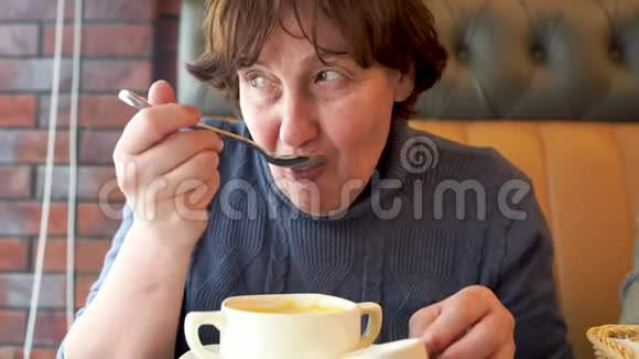 成熟的女人在咖啡馆里吃奶酪奶油汤年长的女性坐在餐馆的桌子上试着喝嫩汤视频的预览图