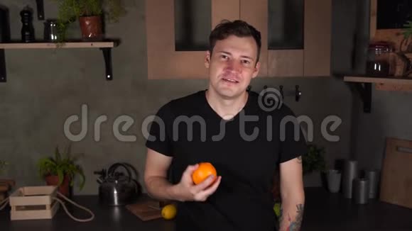 英俊的年轻人用手扔橘子晚上在厨房玩水果时微笑的雄性的肖像视频的预览图
