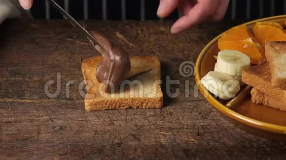 的手用铁刀在一块烤面包上涂抹巧克力酱然后把香蕉片放在上面视频的预览图