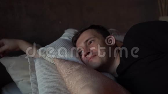 英俊的年轻人清晨躺在床上微笑的男性在床上躺在枕头上时向远处看的肖像视频的预览图