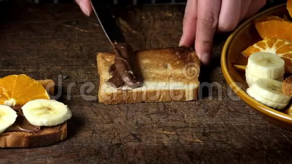 的手用铁刀在一块烤面包上涂抹巧克力酱然后把香蕉片放在上面视频的预览图