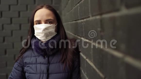 戴着医疗面具的年轻女子脸上贴着黑色砖墙的肖像成年女性用面具遮住她的脸视频的预览图