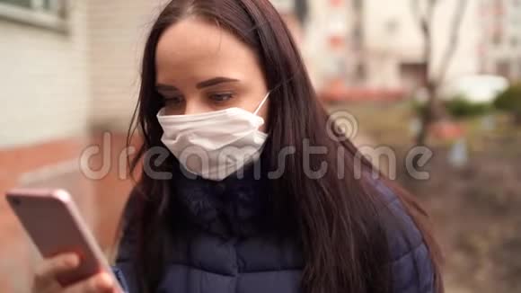 年轻女子戴着医用口罩在院子里街上的手机上得知疫情成年女性视频的预览图
