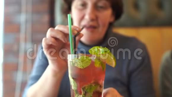 成年妇女在咖啡馆喝鸡尾酒成年女性坐在餐桌上用吸管啜饮新鲜水果饮料视频的预览图