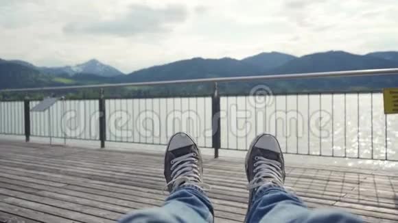 人的双腿穿着著名的运动鞋躺在湖边码头欣赏山景视频的预览图
