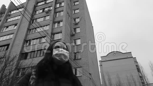 戴着医用面具的年轻女人成年女性在多层楼背景的街道上用面具遮住她的脸视频的预览图