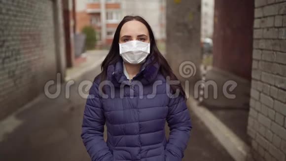 戴着医疗面具的年轻女子站在街上的拱门上的肖像成年女性戴着面罩视频的预览图