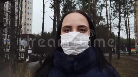 街上院子里戴着医用口罩的年轻女子的肖像成年女性用面具遮住她的脸视频的预览图