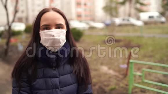 街上院子里戴着医用口罩的年轻女子的肖像成年女性用面具遮住她的脸视频的预览图