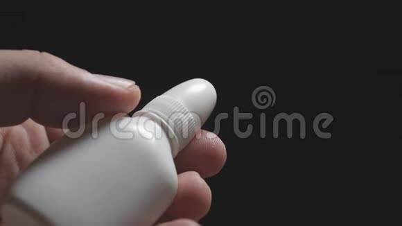 一个人手中的白色瓶子在黑暗背景上特写视频的预览图