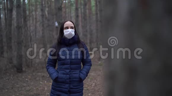 戴着医疗面具的年轻女子的肖像靠在森林里的树上成年女性戴着面罩视频的预览图