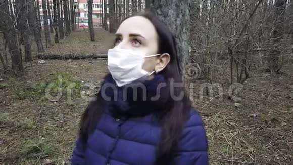 戴着医疗面具的年轻女子的肖像靠在森林里的树上成年女性戴着面罩视频的预览图