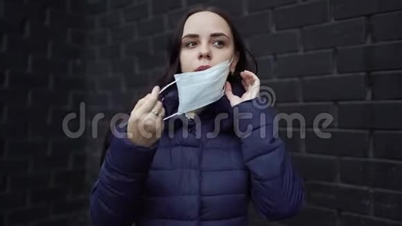 年轻女子脸上戴着医疗面具贴在黑色砖墙上的肖像成年女性遮住了她的脸视频的预览图