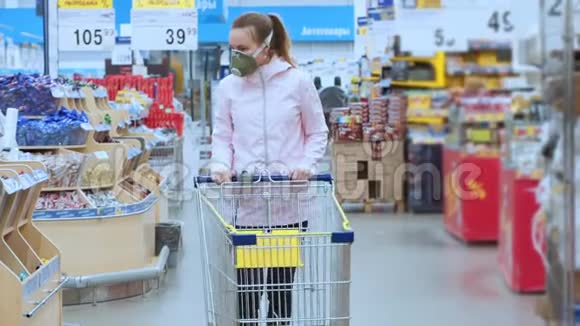 一个戴着医疗面具的悲伤的女人带着购物车在超市里走着个人防护设备视频的预览图