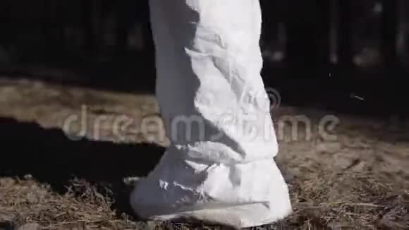 在阳光明媚的日子里在森林或公园里行走时穿着安全套装的腿部特写穿着白色制服的男性病毒学家视频的预览图