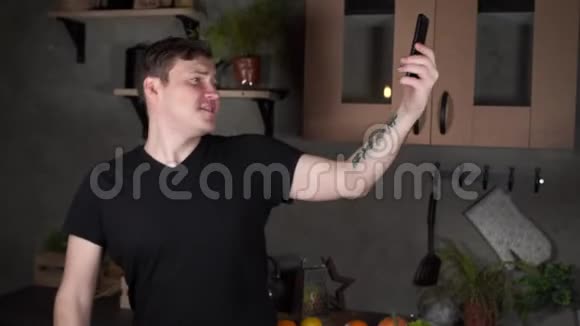 年轻英俊的男人在厨房的智能手机上跳舞和自拍迷人的男性花时间欣赏的肖像视频的预览图
