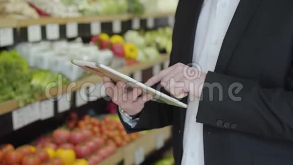在杂货店用平板电脑特写白人男性的手无法辨认的成年男子西装革履使用购物清单视频的预览图