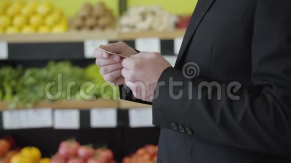 在杂货店里白人男性手拿着钞票的侧视无法辨认的优雅男人穿着西装看着价格视频的预览图