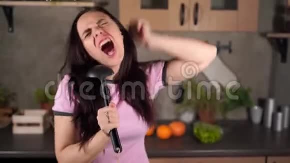 活泼的黑发在厨房里用勺子唱歌喜出望外的黑发女人张开嘴端着黑菜视频的预览图