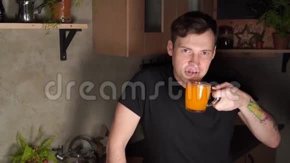 年轻的帅哥在厨房喝橙汁迷人的男性在晚上享受清爽的饮料的肖像视频的预览图