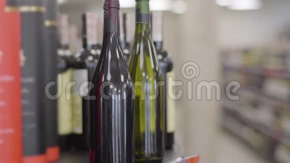 男性白种人手拿一瓶白葡萄酒在架子上一个头脑模糊的成年男子走在酒精的货架上视频的预览图