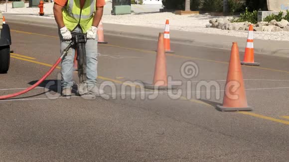 作为公用事业项目的一部分当一名工人在一条城市街道的沥青路面上用手提电锤工作时灰尘从机器上飞了下来视频的预览图
