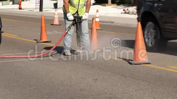 作为公用事业的一部分工作人员在橙色安全警示锥旁边的一条城市街道的沥青上使用了一把手提锤视频的预览图
