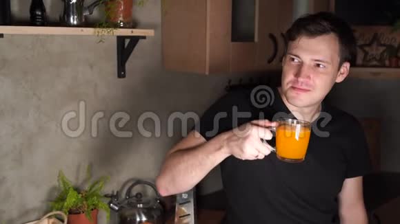 一个男人在厨房里喝橙汁在厨房里喝果汁的年轻男性的肖像视频的预览图