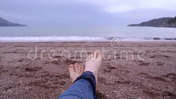 穿着牛仔裤的人腿躺在沙滩上脚趾在移动视频的预览图