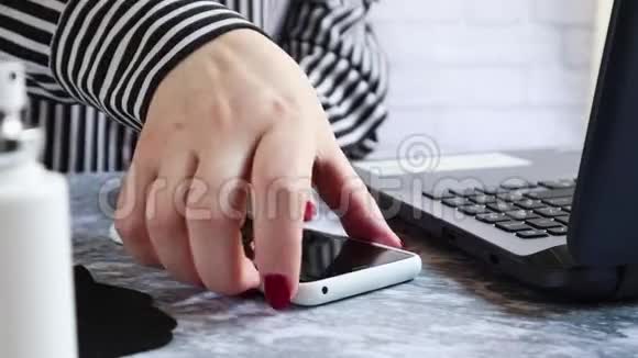 一名妇女在家里或办公室里坐在桌子旁消毒智能手机的表面以防止冠状病毒的传播视频的预览图
