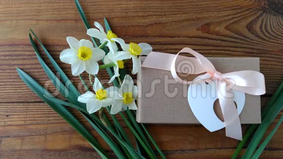 白色水仙花和棕色礼盒贺卡用粉色丝带放在木质背景4K视频上女人的手放花视频的预览图