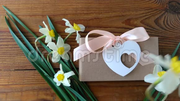 白色水仙花和棕色礼盒贺卡用粉色丝带放在木质背景4K视频上女人的手放花视频的预览图