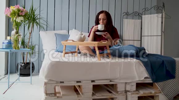早上穿着睡衣躺在床上的年轻迷人的女人漂亮的女人坐在家里的大床上喝咖啡视频的预览图