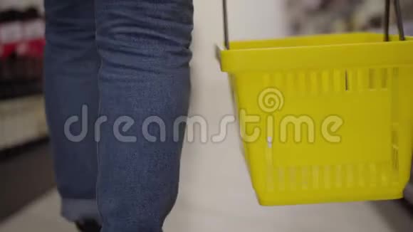 穿着牛仔裤的人用黄色购物篮沿着超市货架走着特写镜头照相机视频的预览图