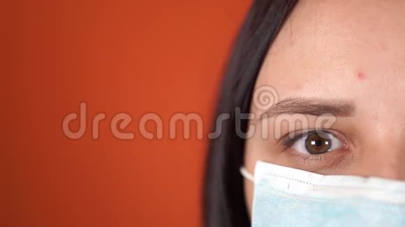 橙色背景下脸上戴着医疗面具的女人冠状病毒的流行视频的预览图