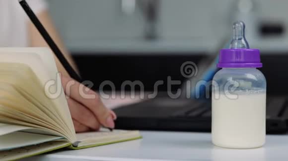 检疫期间厨房里的年轻女子女性手在笔记本电脑键盘上打字在笔记本上写笔记视频的预览图
