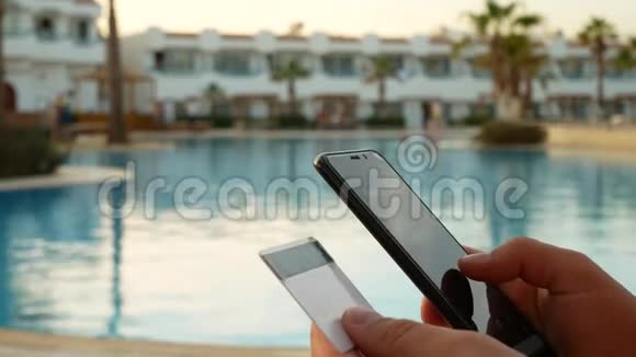 在游泳池附近用智能手机和信用卡在线购买视频的预览图