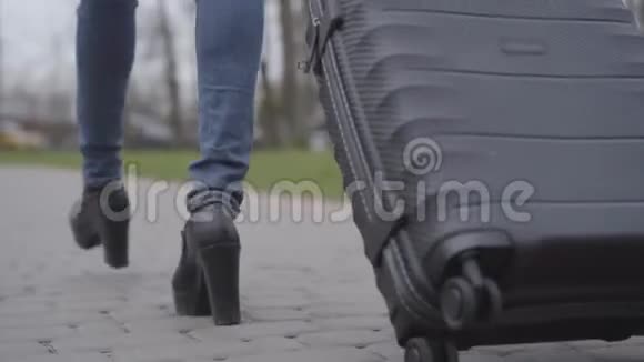 镜头跟随女腿在高跟鞋和牛仔裤走在公园小巷与旅行袋无法辨认的苗条女人视频的预览图